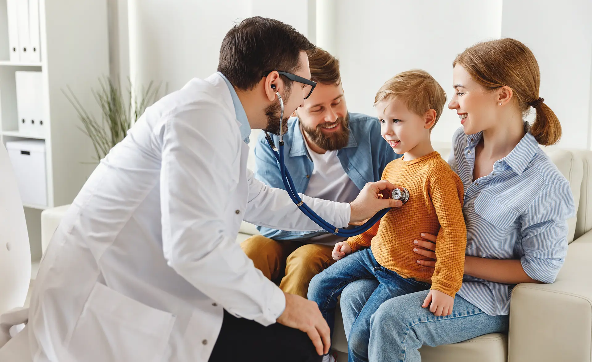 doctor listening to a young boys heart while he sits on is mother's lap